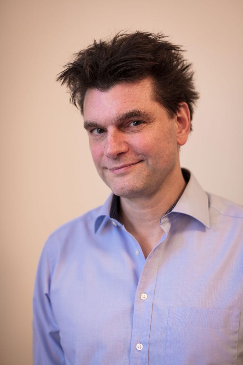 Lutz van der Horst (Mann mit dunklen, etwas struppig hochgegelten Haaren in einem hellblauen Hemd) blickt freundlich lächelnd in die Kamera.